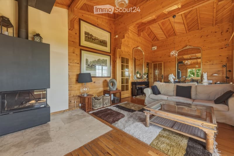 Cozy living room with exposed wooden beams, a large fireplace, a beige sofa, a glass coffee table, and wooden side tables.
