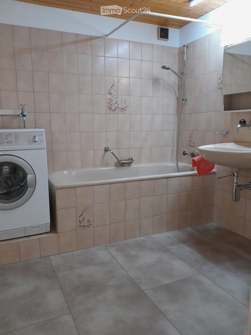 Bathroom with beige tiled walls, a bathtub, a sink, and a washing machine. Features a floral tile design and a window for natural light.