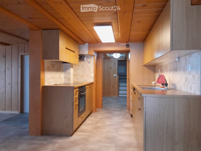 A narrow hallway with wooden walls and ceiling, leading to a kitchen area with wooden cabinets, a stove, and a sink.
