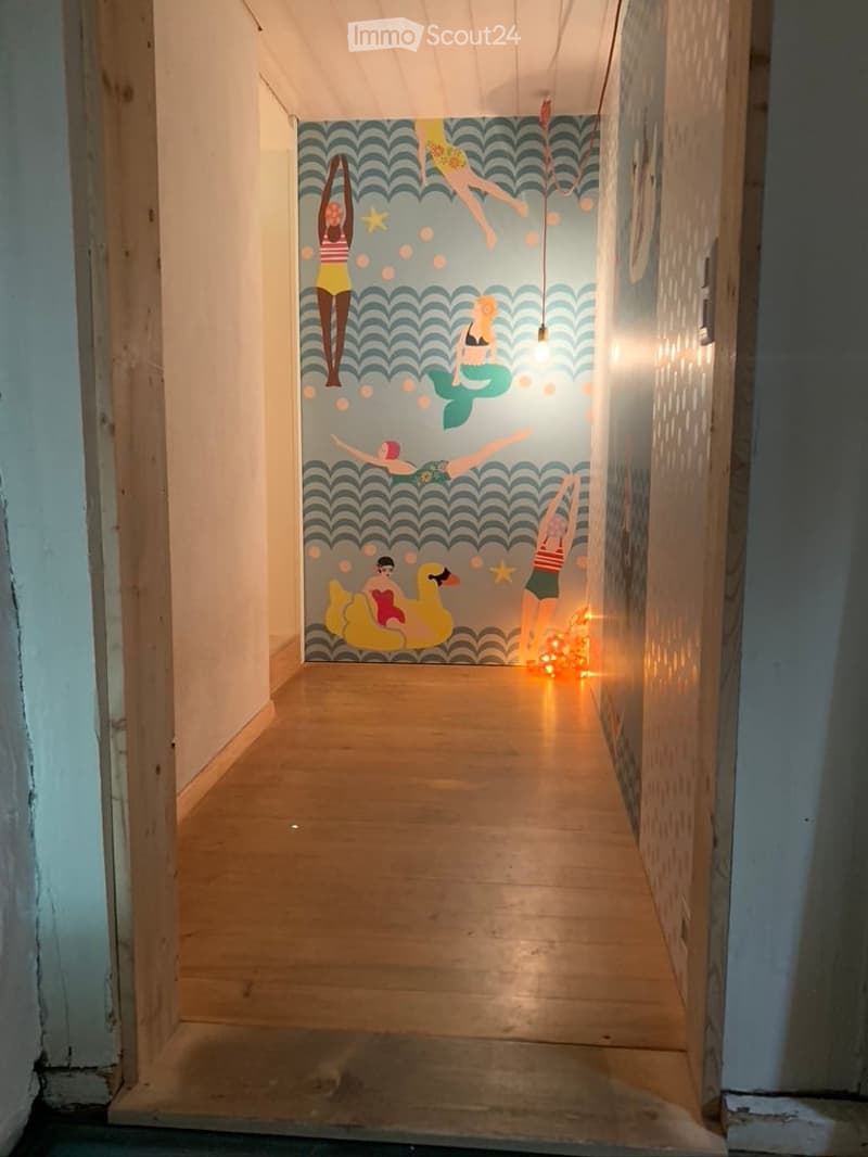 A narrow hallway with wooden flooring and a vibrant mural featuring mermaids and sea-themed illustrations. The lighting is warm and inviting, creating a cozy atmosphere.