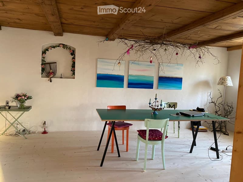Bright dining area with a green table, colorful chairs, laptop, candle holder, vase with flowers, and artwork on the walls.