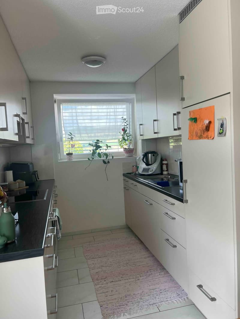 Modern kitchen with white cabinets, stainless steel appliances, and a window with blinds. Includes a sink, blender, and various kitchen items on the counters.