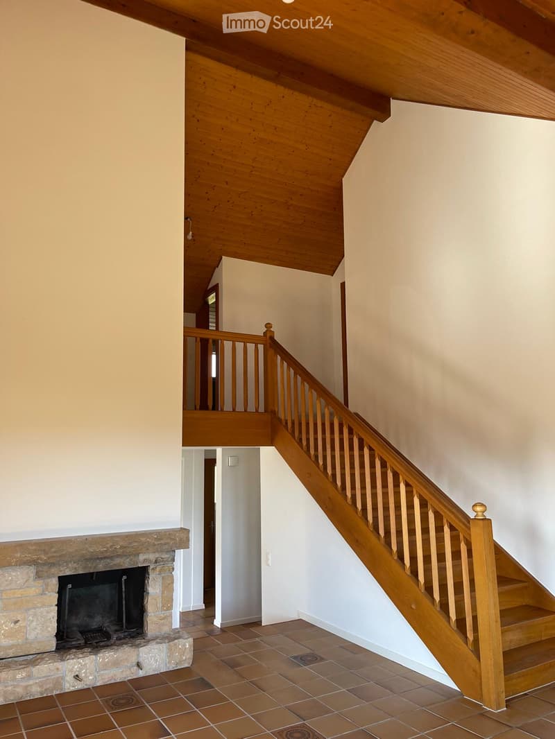 Wooden staircase with a wooden railing leads to an upper level. A stone fireplace is visible on the left side of the hallway.