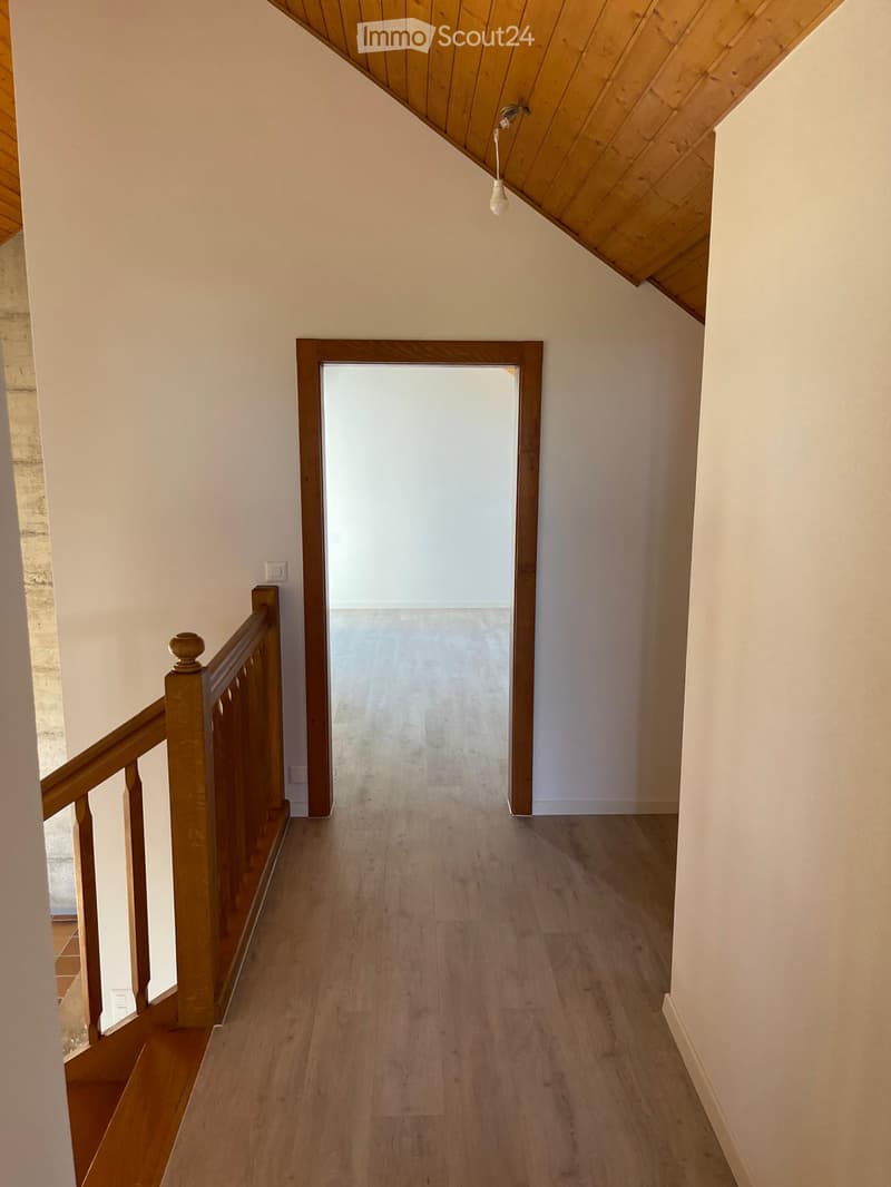 Empty hallway with wooden flooring, white walls, and a wooden railing leading to an open doorway.