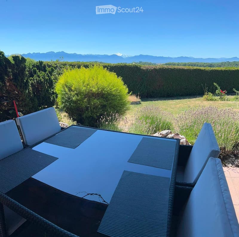 Outdoor patio with a table and chairs, surrounded by greenery and a scenic mountain view in the background.