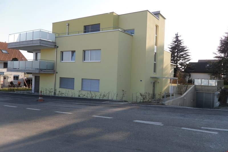 Modern two-story building with light yellow facade, multiple windows, and a balcony on the upper floor.