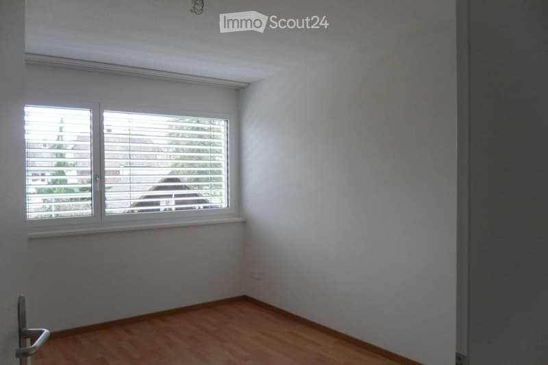 Empty room with light-colored walls, wooden flooring, and a window with blinds. No furniture or equipment is present.
