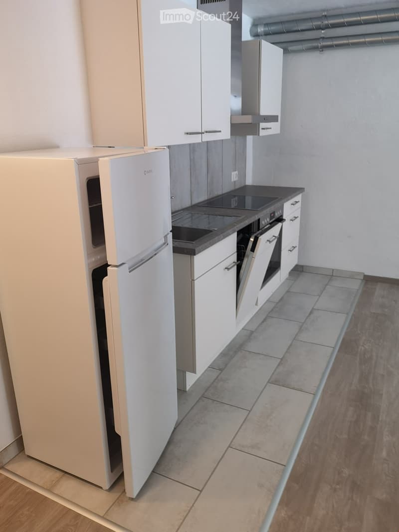 Modern kitchen with white cabinets, a refrigerator, and an oven, featuring a dark countertop and tiled backsplash.