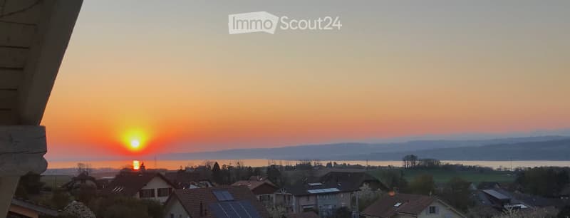 Balcony view overlooking a town with houses, solar panels, and a lake during sunset.