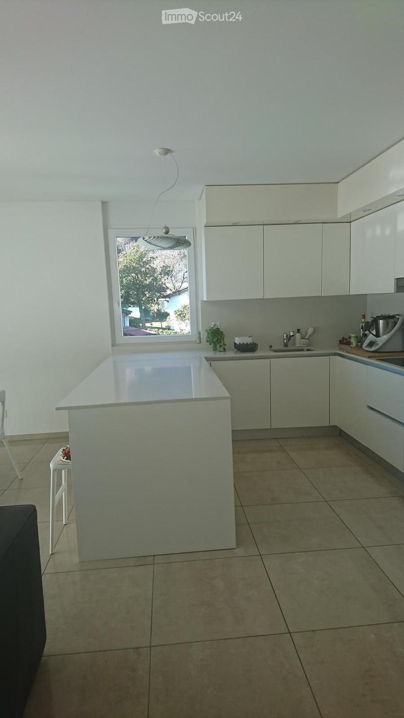 Modern kitchen with white cabinets, a central island, and a window overlooking a garden. Includes a sink, faucet, and various appliances.