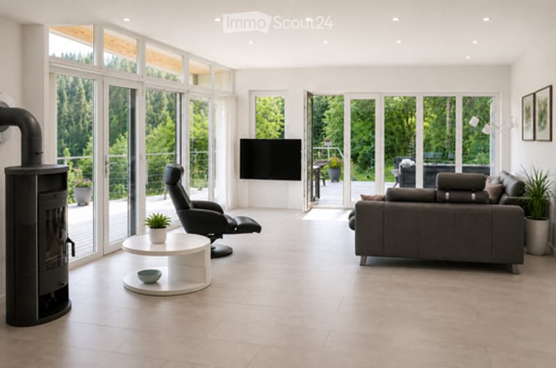 Modern living room with large windows, fireplace, grey sofa, coffee table, armchair, TV, and plants.