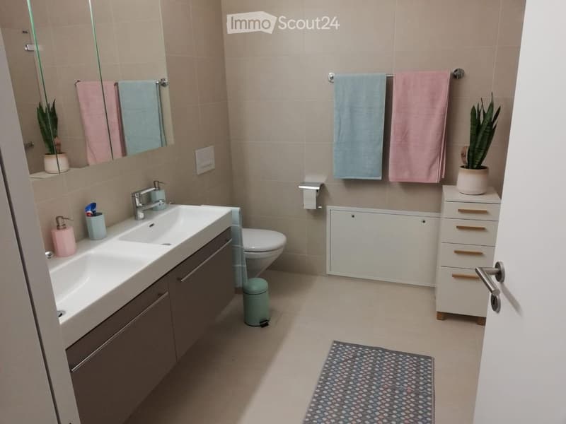 Modern bathroom with a double sink, toilet, mirror, towel rack, and small potted plants on the cabinets.