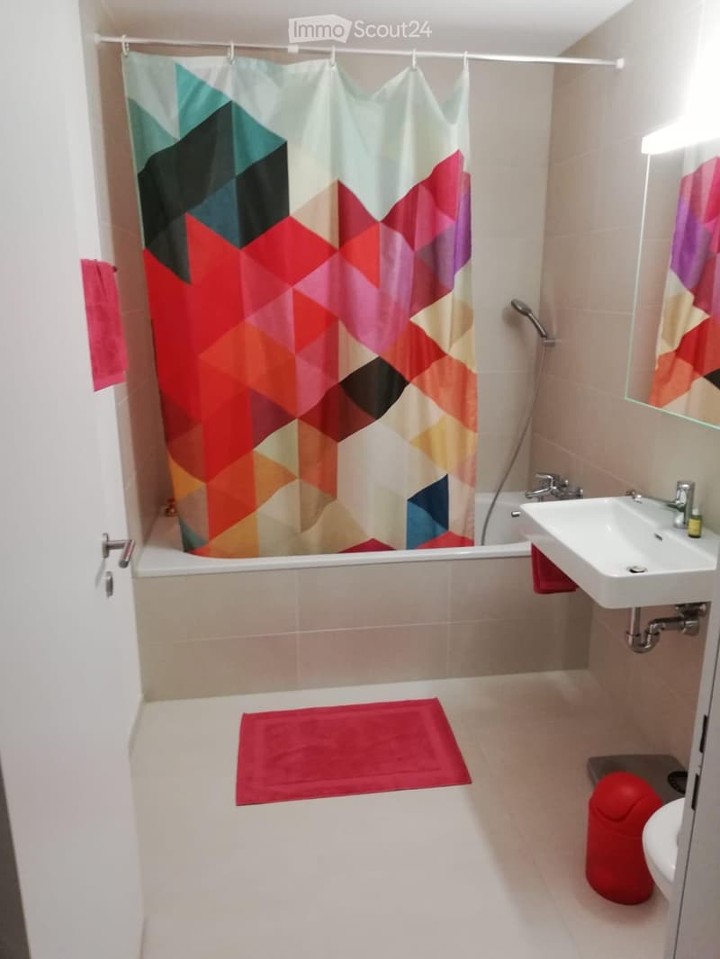 Modern bathroom with a bathtub, sink, mirror, toilet, and a colorful geometric shower curtain.