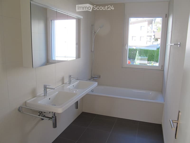 White bathroom with bathtub, double sinks, mirror, and windows.