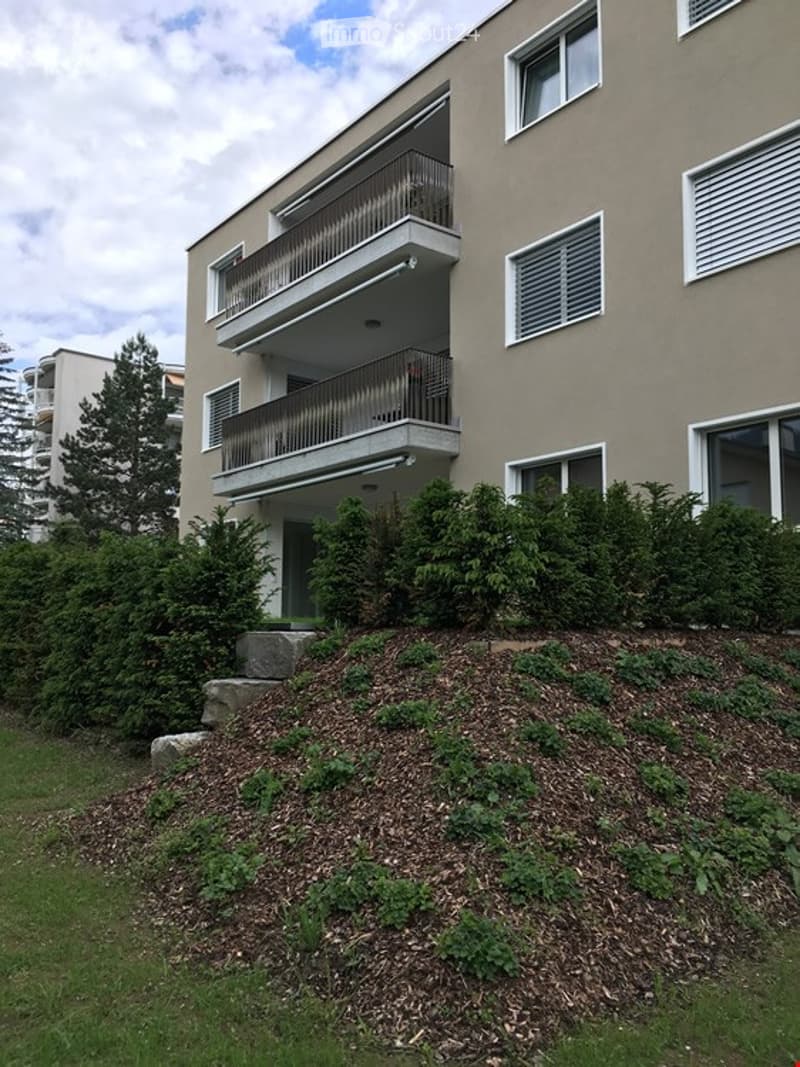 Three story building with balcony, large grass and bushes at the entrance
