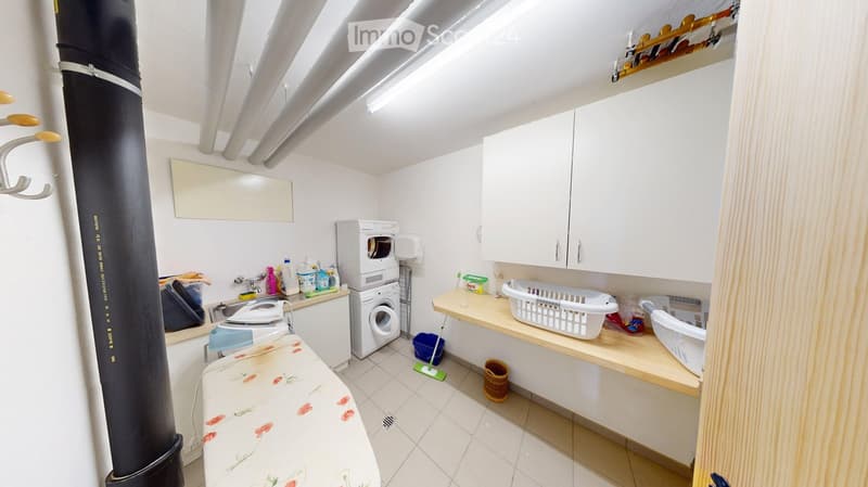 Well-lit bathroom with a washing machine and dryer, sink, mirror, cabinet, laundry baskets, ironing board, and cleaning supplies.