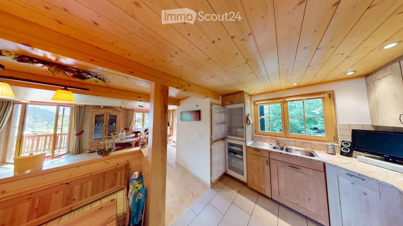 Cozy kitchen with wooden beams, white cabinets, stainless steel sink, refrigerator, and a dining area with a table and chairs.