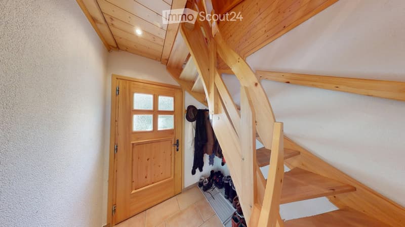 Wooden staircase leading upwards, wooden door with glass panels, coats and shoes stored in a niche, exposed wooden beams on the ceiling.