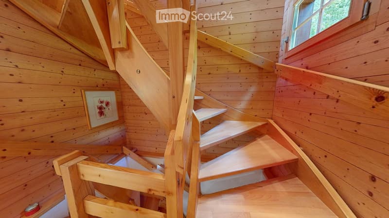 Wooden staircase with white steps and handrails, leading up to a landing with a window and a framed picture on the wall.