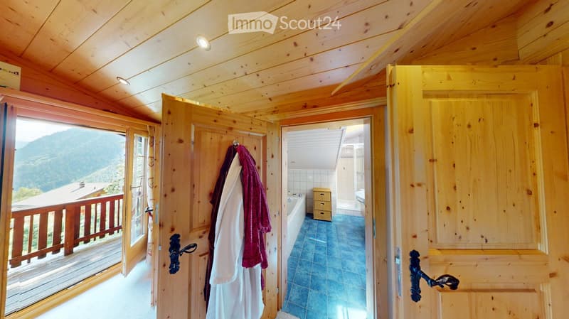 Cozy wooden bathroom with a bathtub, toilet, and a small storage unit. The room features exposed wooden beams and a view of the mountains through a large window.