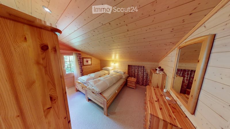 Cozy wooden bedroom with slanted ceiling, single bed with white bedding, nightstand, mirror, wardrobe, and picture frame on wall.