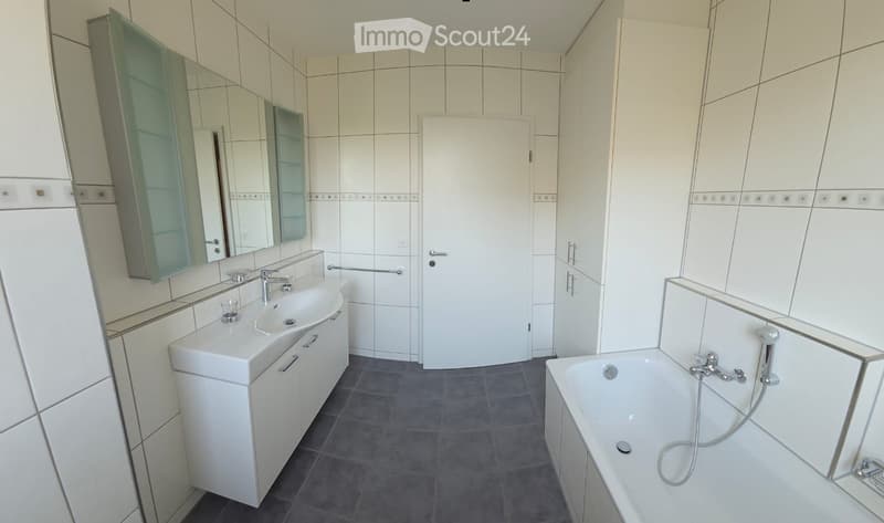Modern bathroom with white tiles, a white sink with a cabinet, a bathtub, and a large mirror with glass-fronted cabinets.