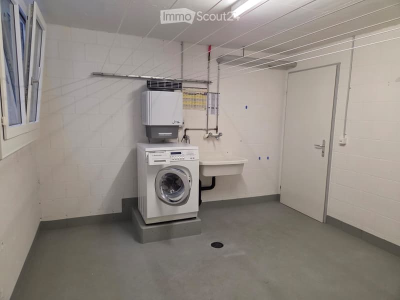 Utility bathroom with a washing machine, sink, and faucet, featuring white brick walls and a concrete floor.