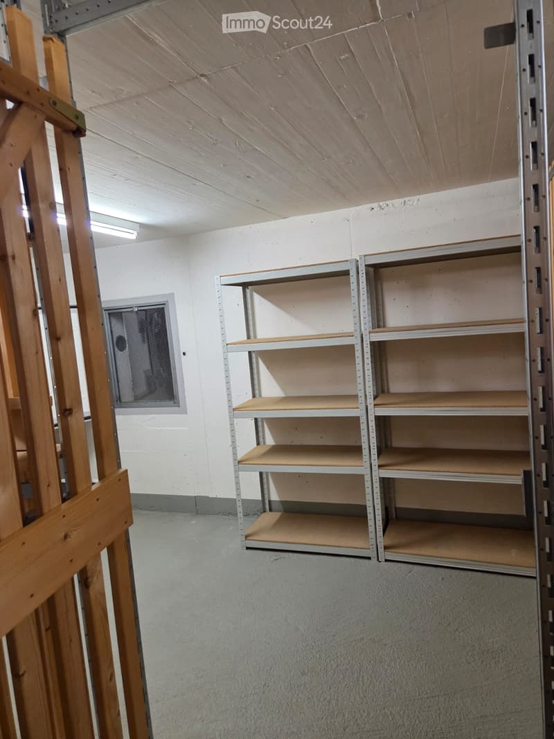 Empty storage room with metal shelving units, white walls, and a concrete floor. The shelving units have multiple empty wooden shelves.