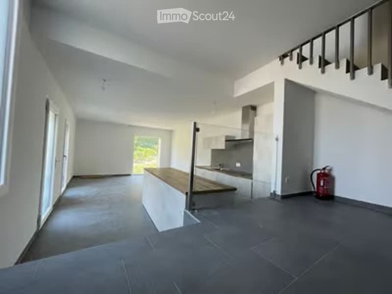 Open-plan unfurnished space with modern design, grey tiled floor, white walls, large windows, and a staircase leading to an upper level.