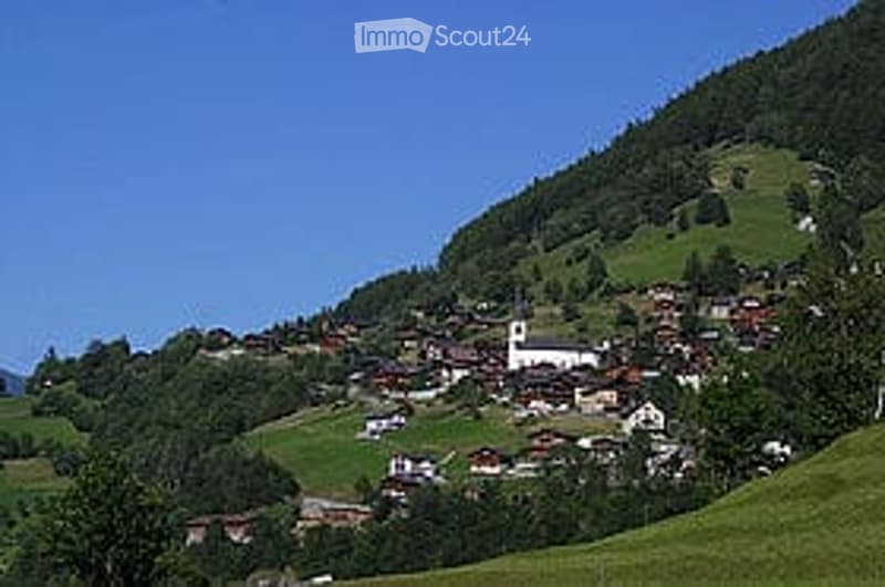 A picturesque village nestled in a valley with scattered houses, a church, and lush green hills under a clear blue sky.