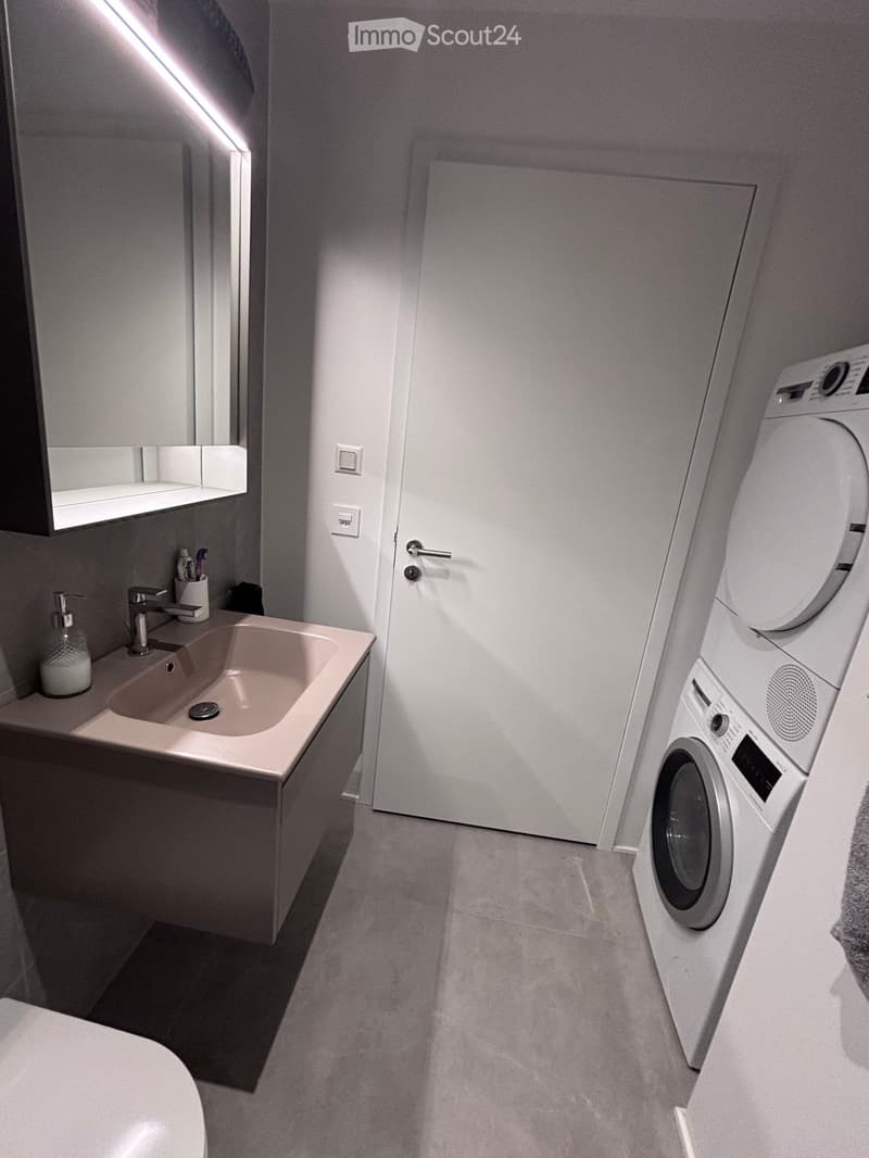 Modern bathroom with a sink, faucet, mirror, and a stacked washing machine and dryer unit.