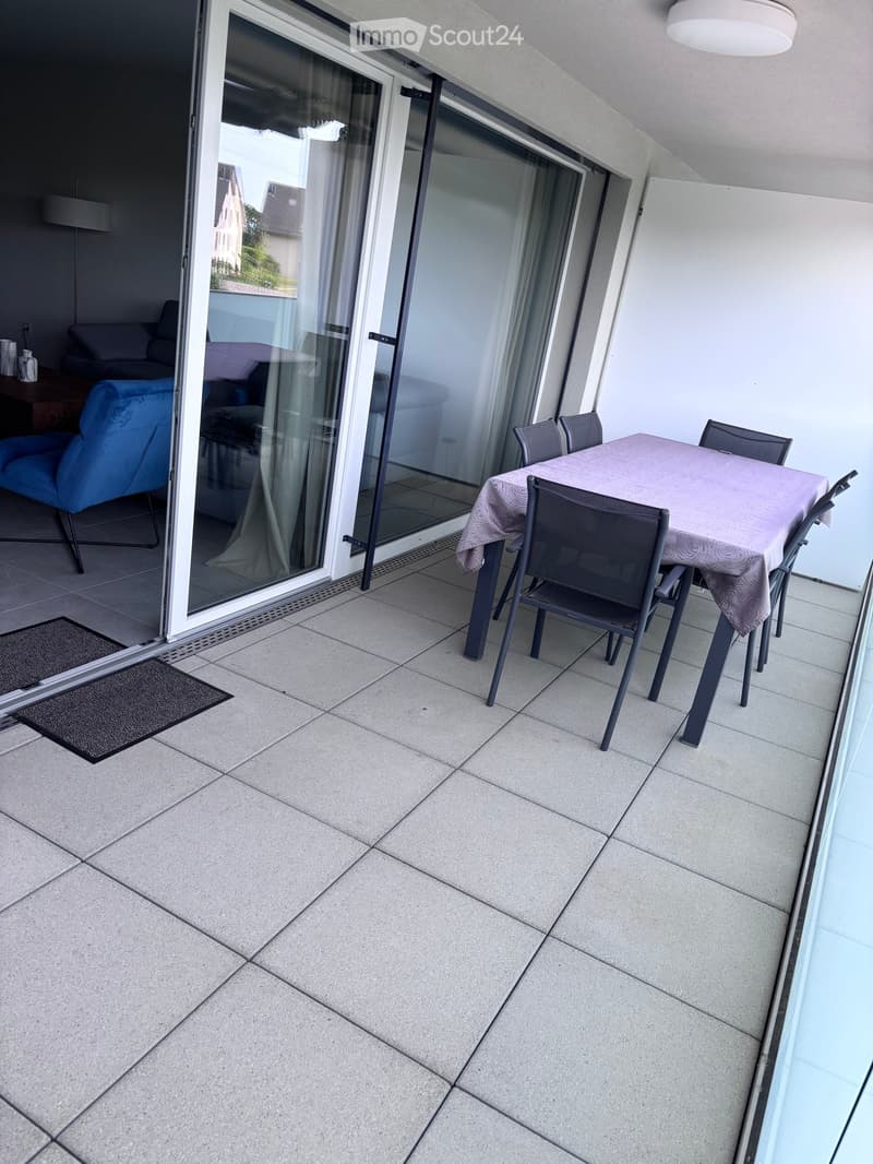 Balcony with tiled floor, glass sliding doors, a small table with chairs, and a blue armchair visible through the open door.