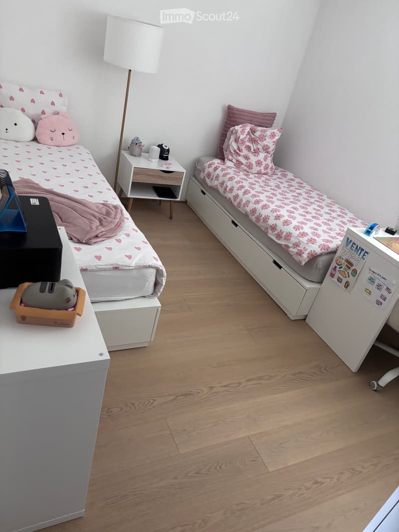 Cozy twin-sized bedroom with two beds, nightstands, and decorative pillows. Features a wooden floor and modern furniture.