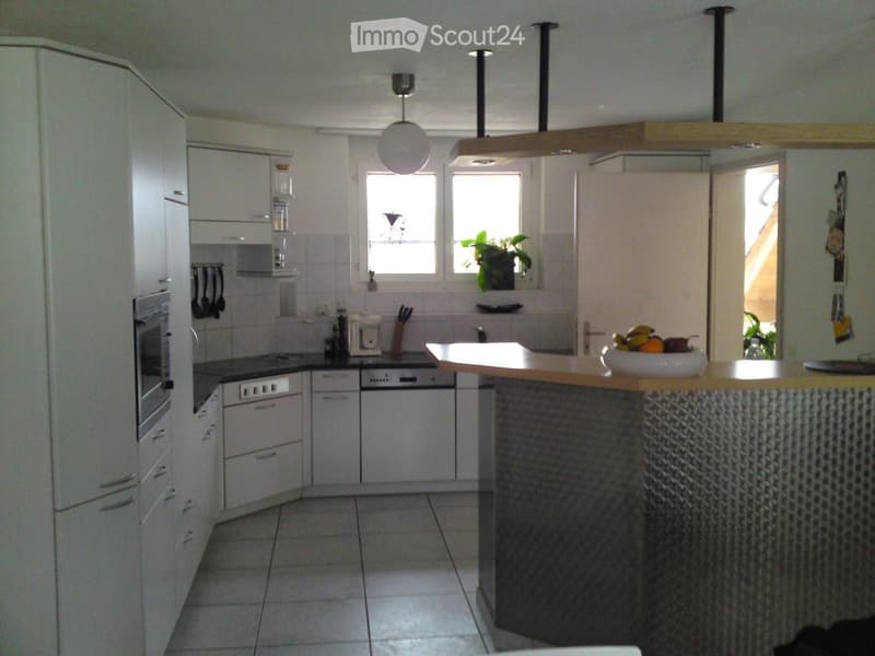 Modern kitchen with white cabinets, stainless steel appliances, a central island with a bowl of fruit, and pendant lighting.