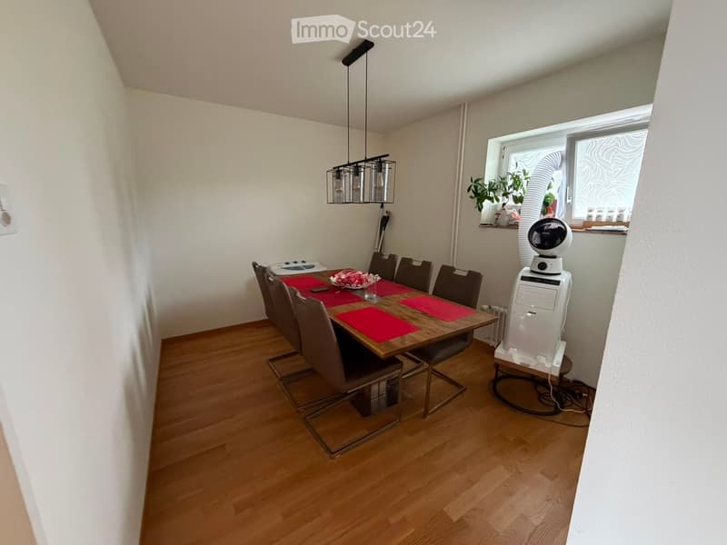 Dining room with wooden floor, dining table, six chairs, red placemats, a fan, a computer tower, and a hanging light fixture.