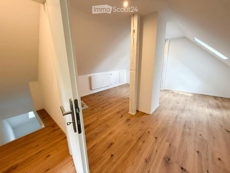 Empty hallway with wooden flooring, white walls, and a door leading to another room. The space is clean and unfurnished.
