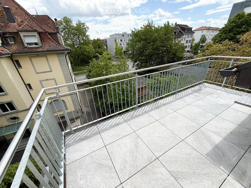 Balcony with tiled floor and metal railing, overlooking a residential area with trees and buildings.