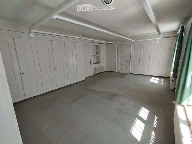 Empty room with white walls, carpeted floor, built-in white cabinets, and a radiator. No furniture or personal items are present.