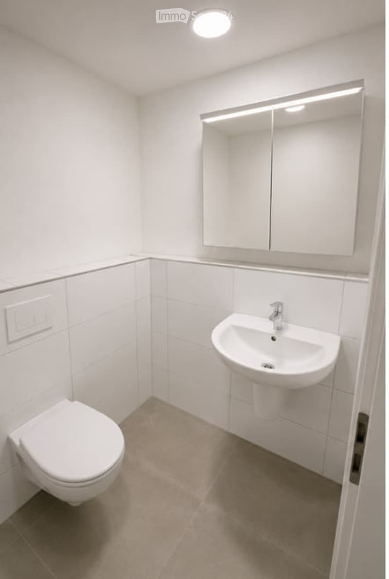 Modern bathroom with white tiles, a toilet, a sink, and a large mirror with integrated lighting.
