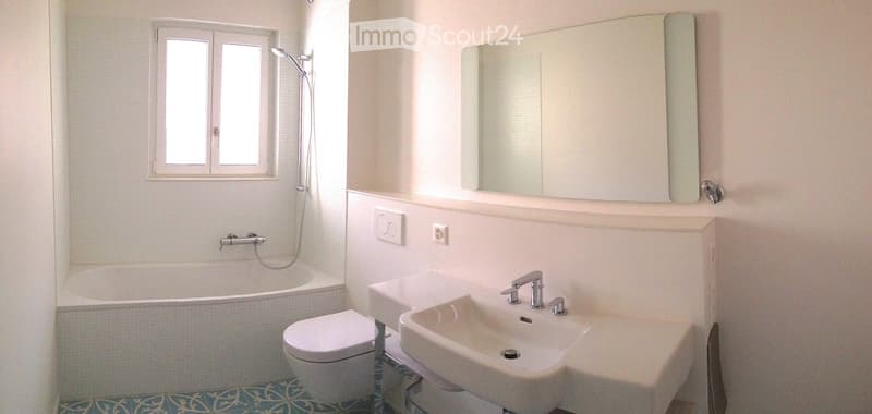 Modern bathroom with white tiled walls, a bathtub, toilet, double sink, mirror, and a showerhead.
