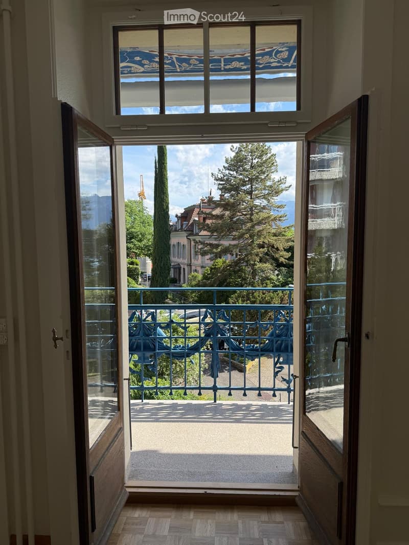 Open balcony with ornate metal railing, overlooking a scenic view of trees, buildings, and mountains.