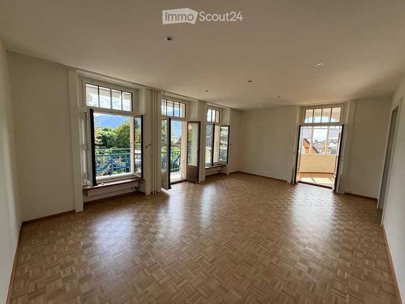 Empty room with wooden herringbone flooring, large windows, and open doors leading to balconies.