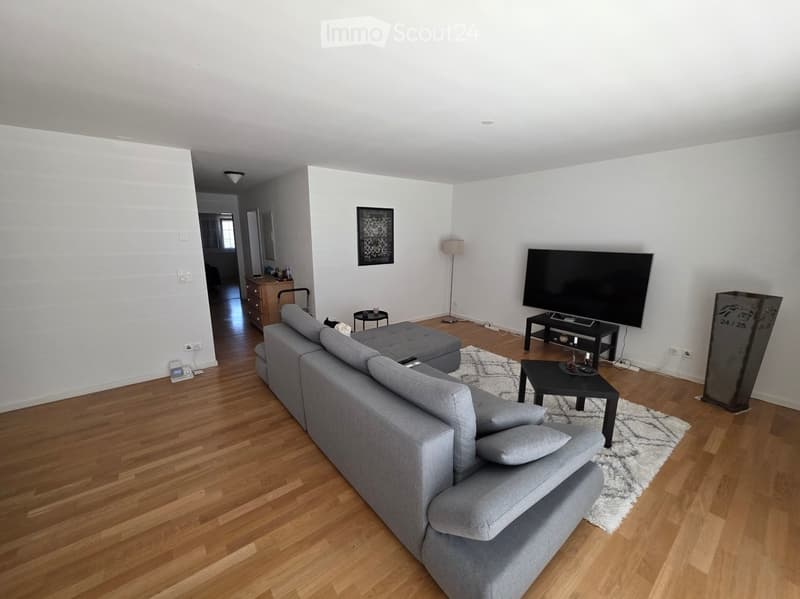 Modern living room with grey sectional sofa, coffee table, TV, floor lamp, and side table. Wooden flooring and white walls.
