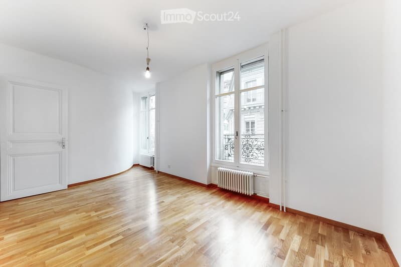 Empty room with wooden flooring, white walls, large windows, and radiators. No furniture or equipment present.