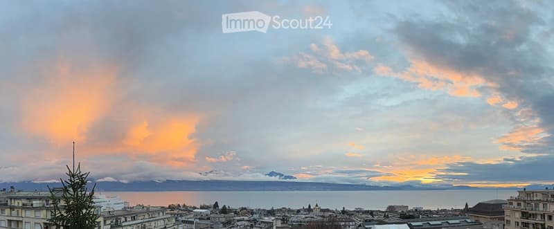 Panoramic cityscape view at sunset, featuring a body of water, distant mountains, and urban buildings.