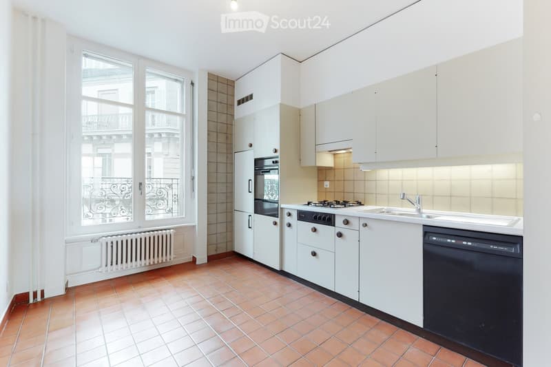 Modern kitchen with white cabinets, stainless steel appliances, and a large window overlooking a balcony.