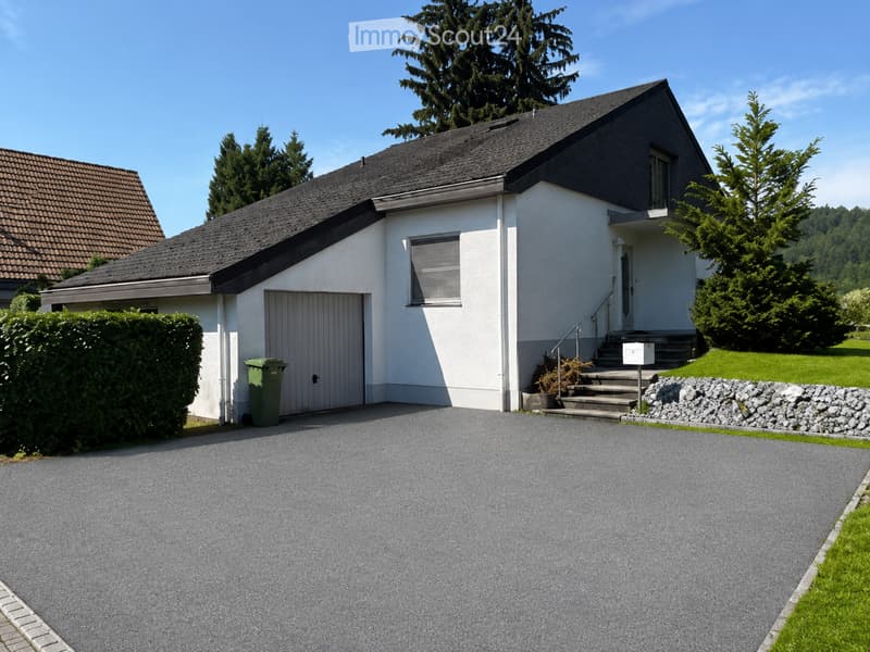 Two-story house with a gray asphalt driveway, garage, and well-maintained garden.