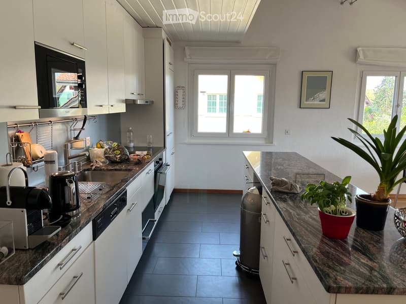 Modern kitchen with white cabinets, granite countertops, stainless steel appliances, and a window overlooking the street.
