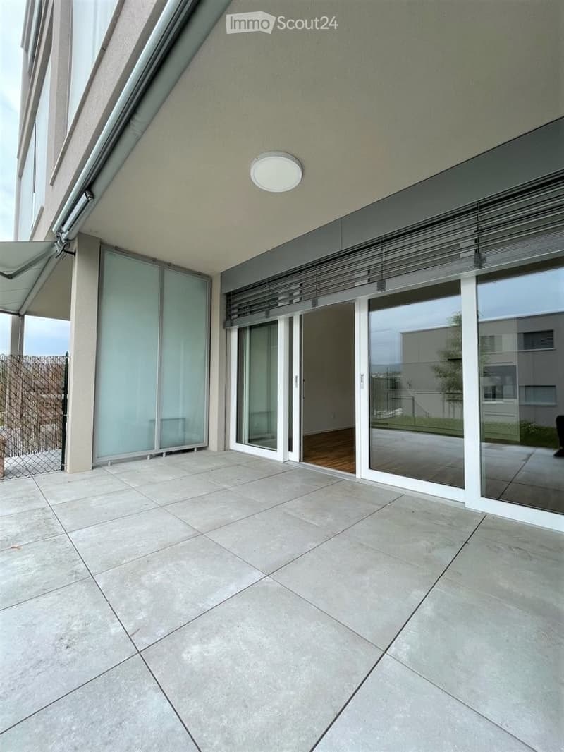 Modern balcony with large glass sliding doors, tiled floor, and a covered section with a light fixture.