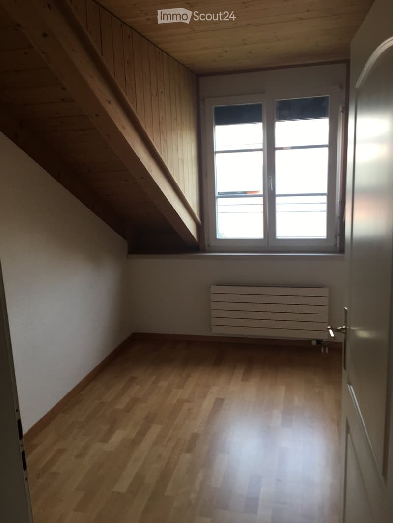 Empty room with wooden flooring, white walls, a window with white frame, and a radiator below the window.
